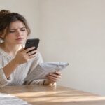 Frustrated shopper at home checking her phone next to a slow China Post poly-mailer parcel