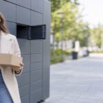 A shopper collecting a parcel at an outdoor locker bank, phone in hand