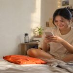 Young woman on her bed checking her phone beside an orange parcel mailer